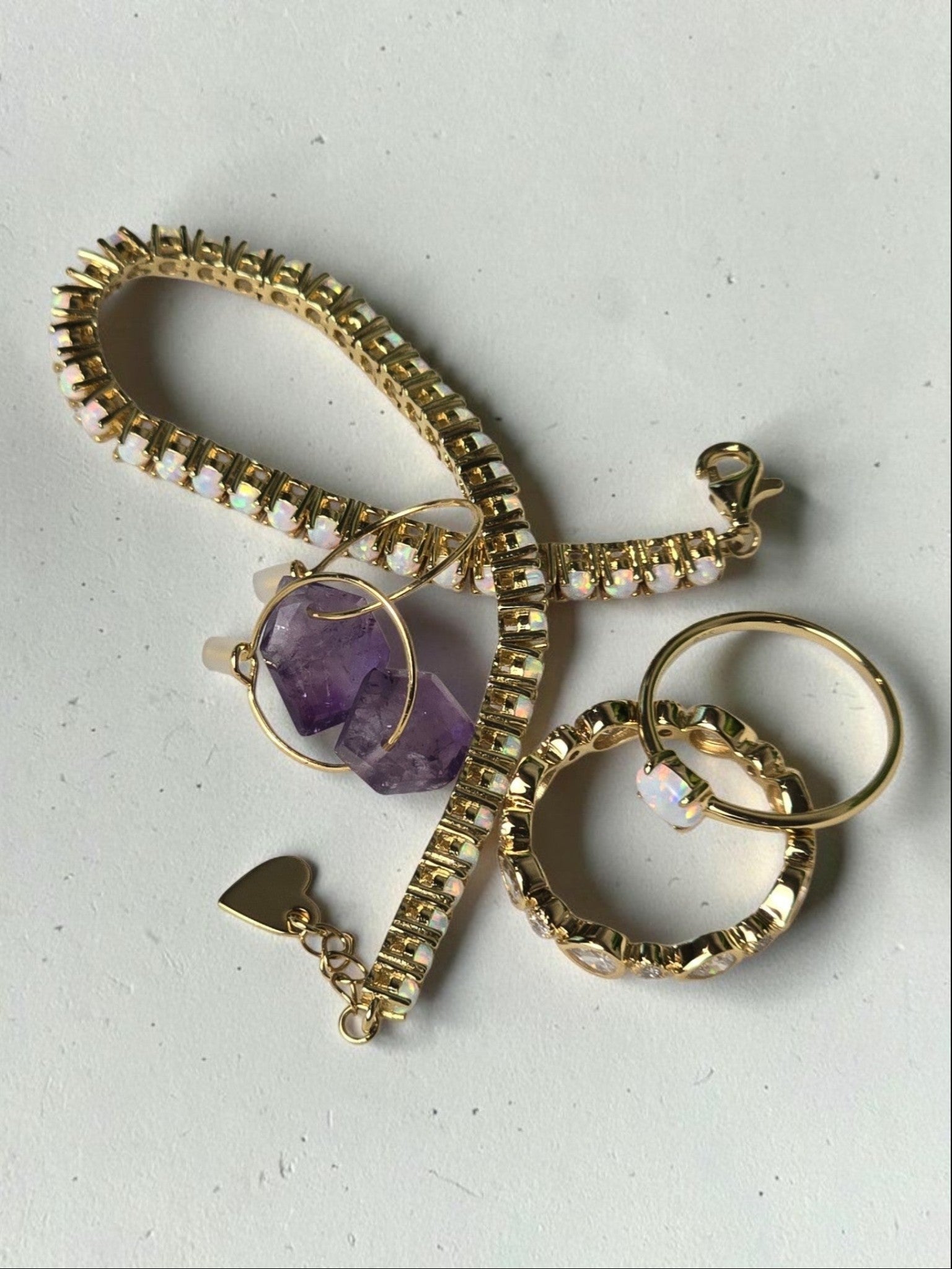reveriebygemma amethyst hoop earrings with gold plated tennis bracelet and opal ring on a textured white surface