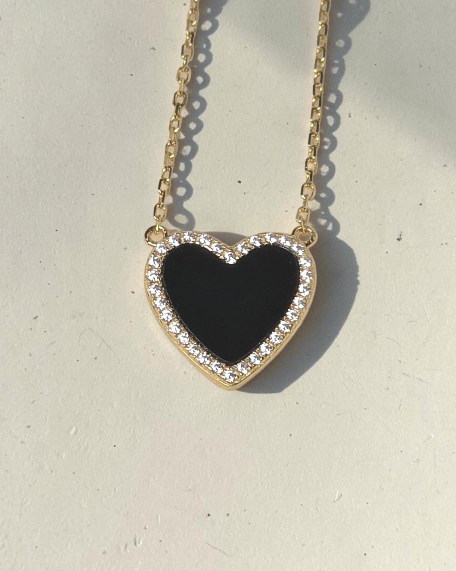 reveriebygemma black onyx heart pendant necklace with a cubic zirconia pave halo on a 14k gold plated silver chain.