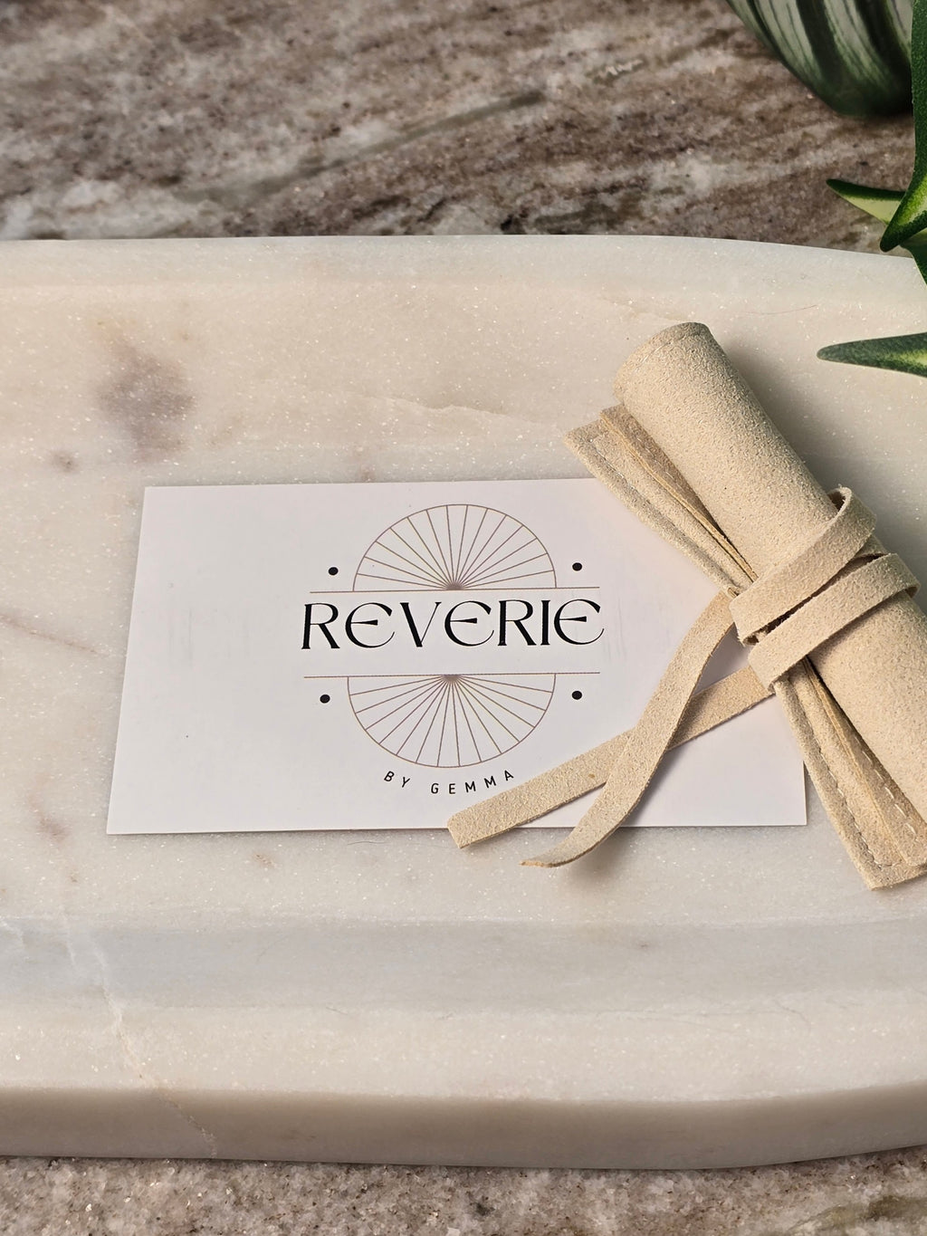 reveriebygemma branded card and beige suede jewelry pouch on a white marble surface