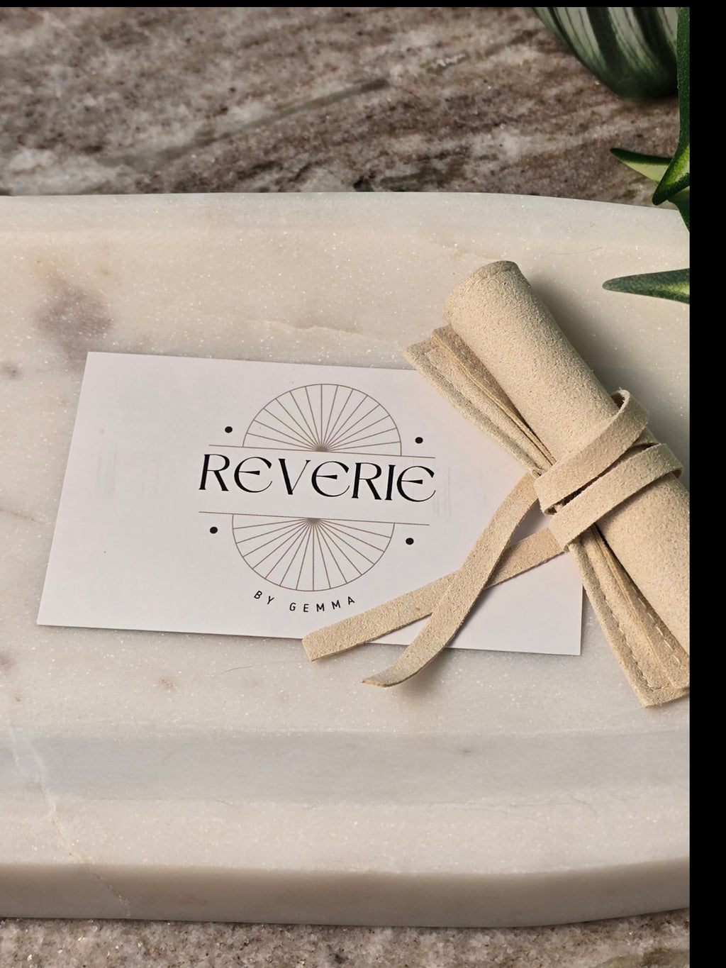 reveriebygemma branded jewelry card and beige suede pouch on a marble surface