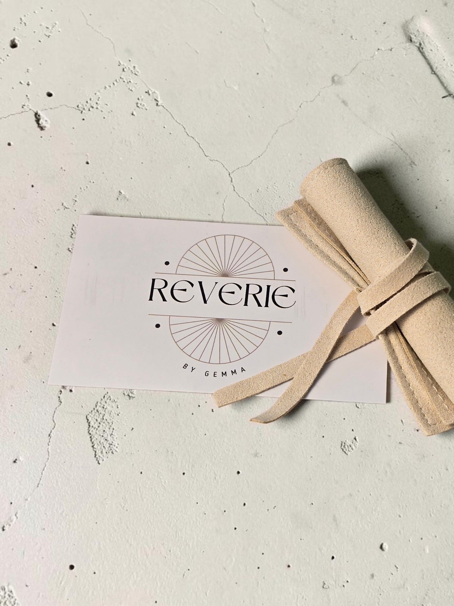 reveriebygemma branded card and beige suede jewelry pouch on a textured white surface