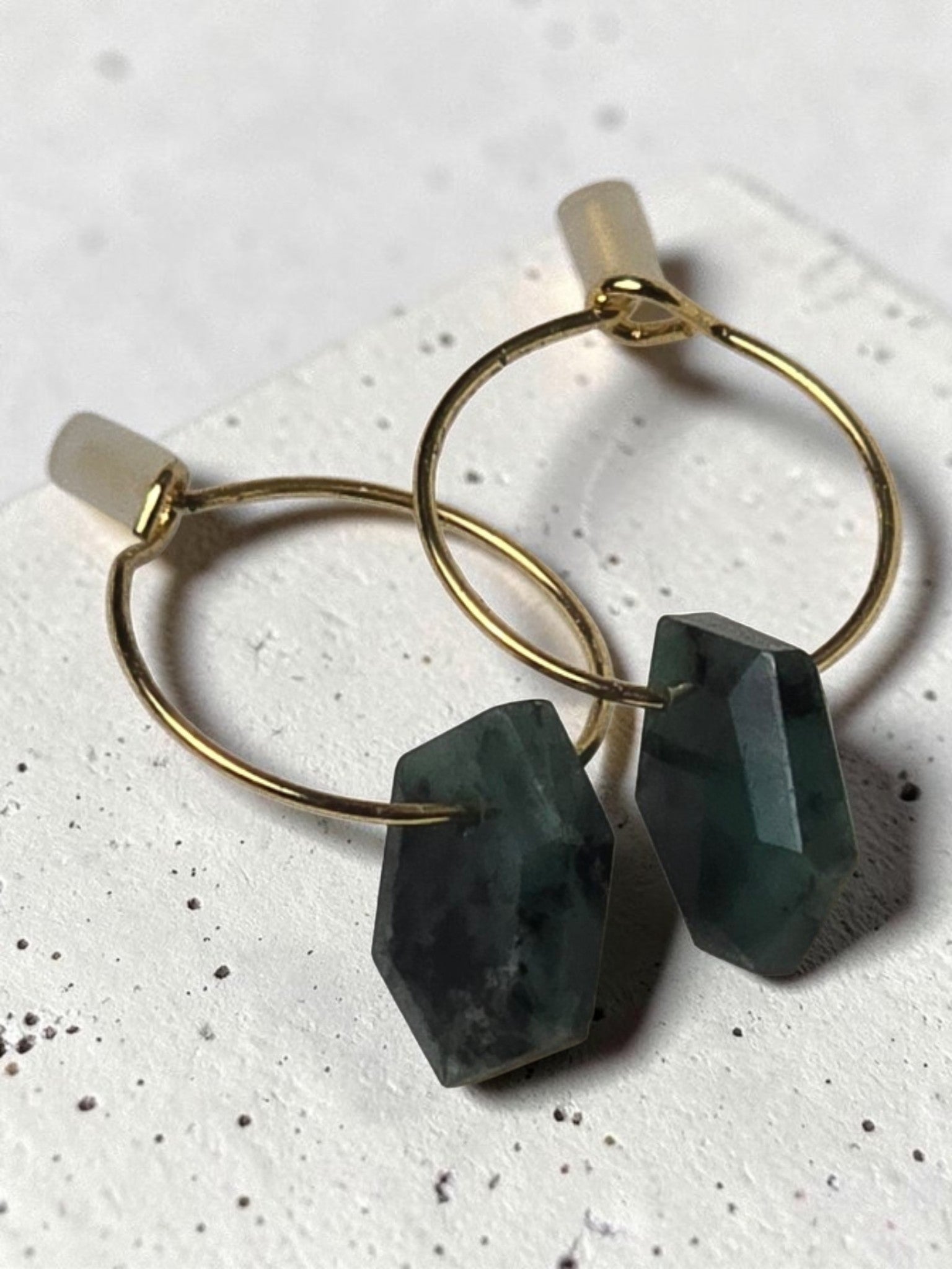 reveriebygemma 14kt gold plated huggie earrings featuring raw geometric emerald gemstone drops on thin gold hoops.