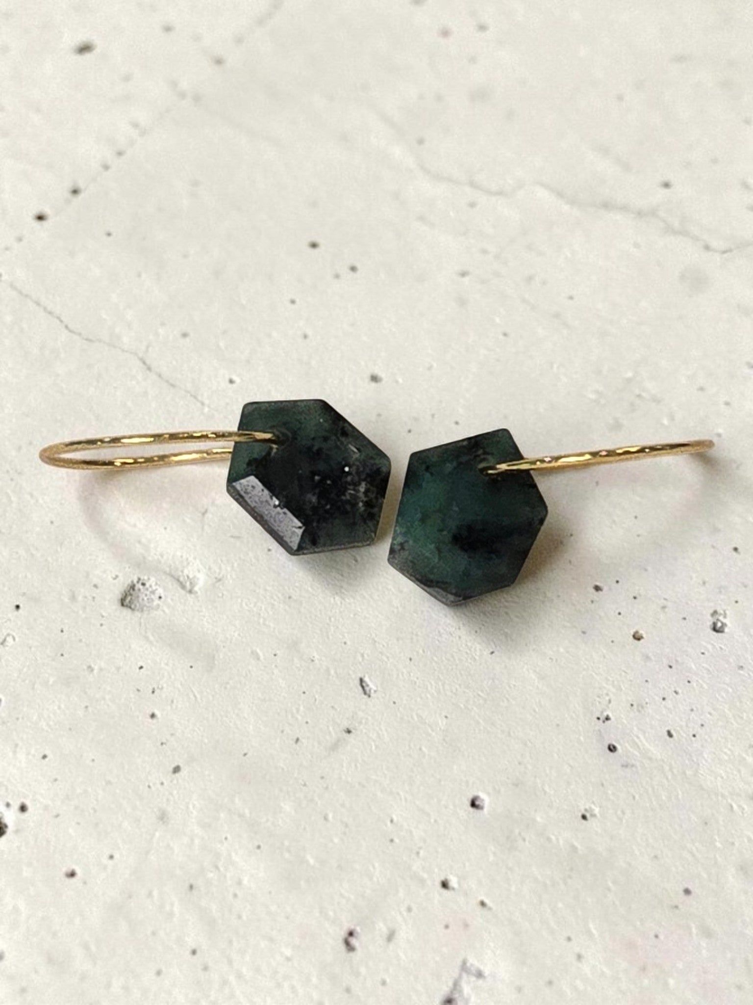 reveriebygemma geometric raw emerald huggie earrings with 14kt gold plated hoops on a marble surface.