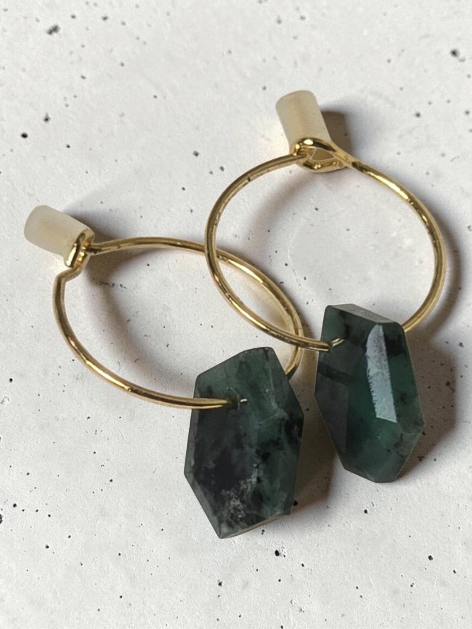 reveriebygemma 14kt gold plated huggie earrings featuring raw, faceted emerald gemstones on minimalist gold hoops.