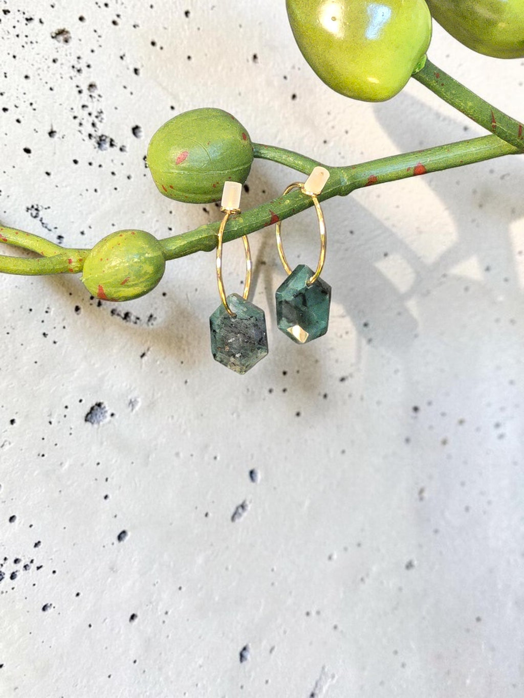 reveriebygemma 14kt gold plated huggie earrings featuring raw geometric emerald gemstones hanging from thin gold hoops.