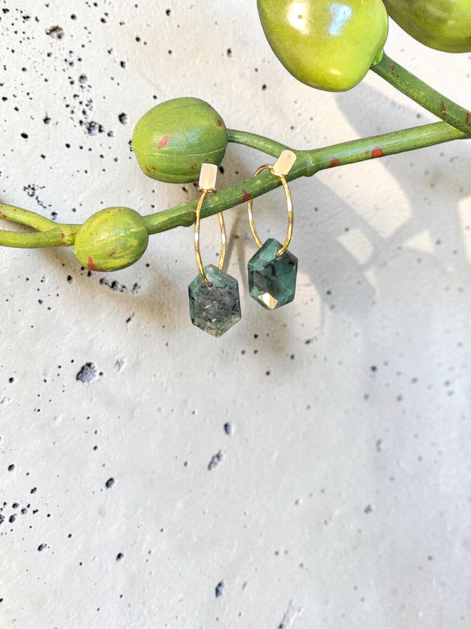 reveriebygemma 14kt gold plated huggie earrings featuring raw geometric emerald gemstones hanging from thin gold hoops.