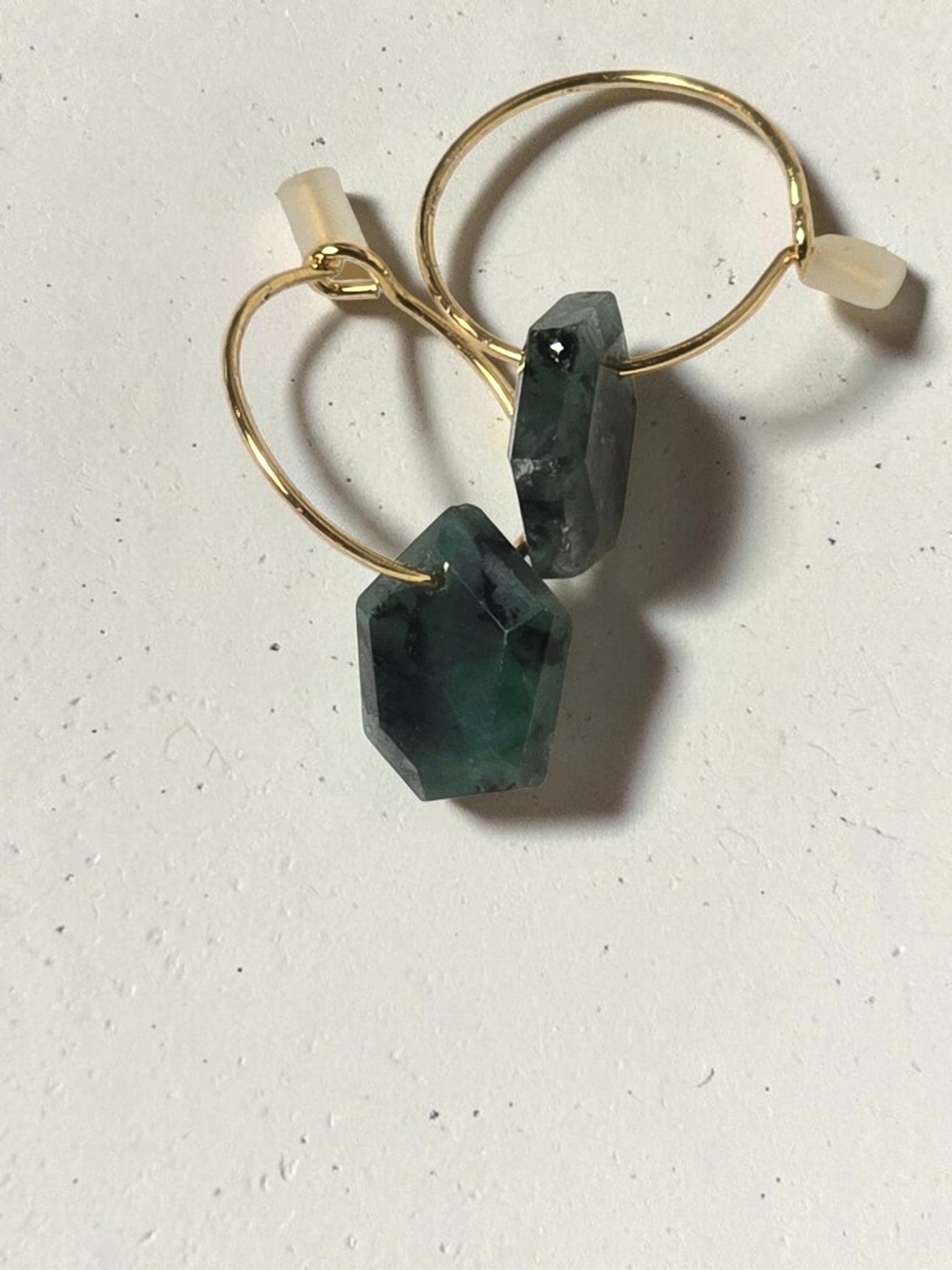 reveriebygemma 14kt gold plated huggie earrings featuring raw geometric emerald gemstones on a marble surface