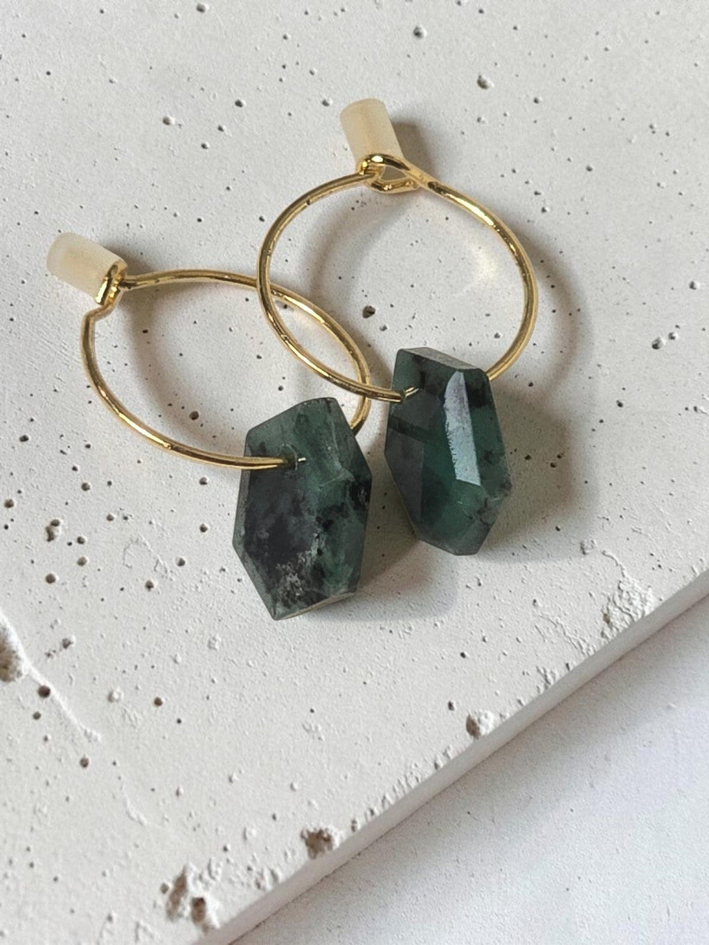 reveriebygemma 14kt gold plated huggie earrings featuring raw geometric emerald gemstones on a light marble surface