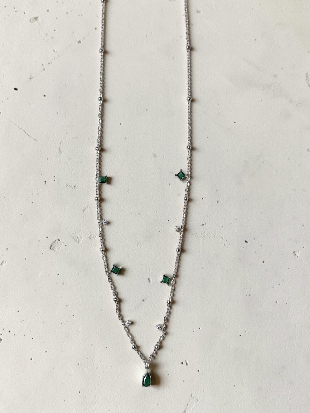reveriebygemma sterling silver choker with green emerald and cubic zirconia tassel charms on a marble background.
