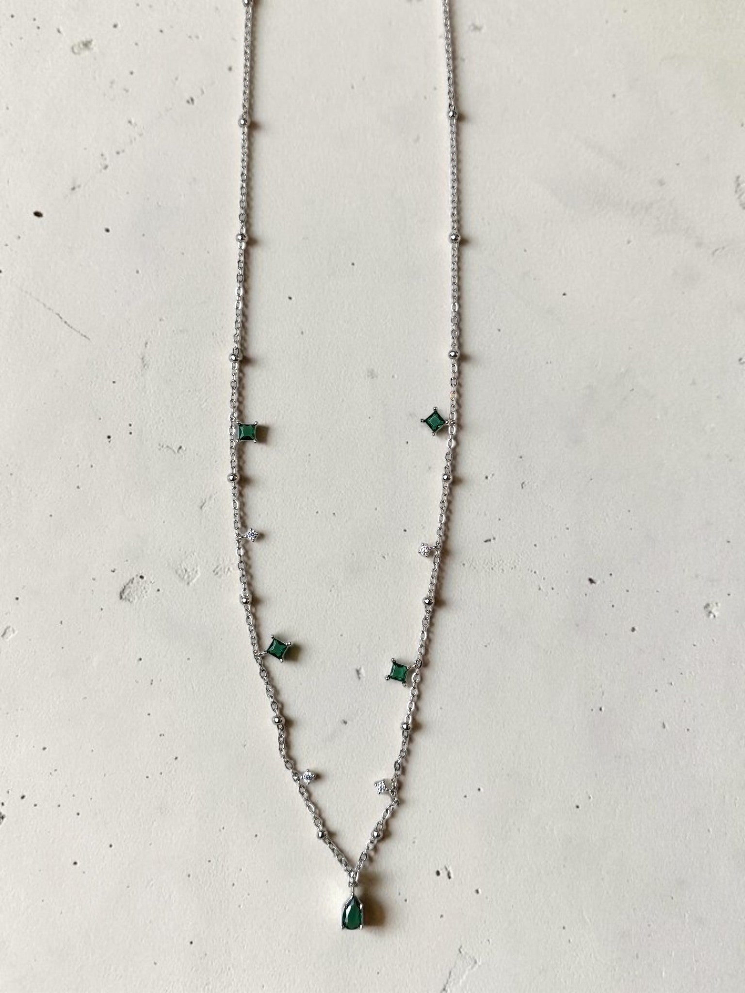 reveriebygemma sterling silver choker with green emerald and cubic zirconia tassel charms on a marble background.