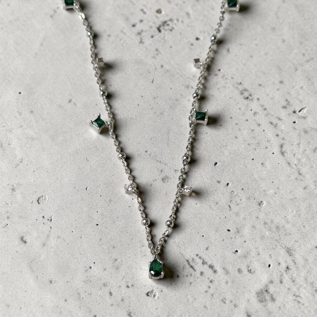 reveriebygemma sterling silver choker with pear-cut emerald and cubic zirconia tassel charms on a marble surface
