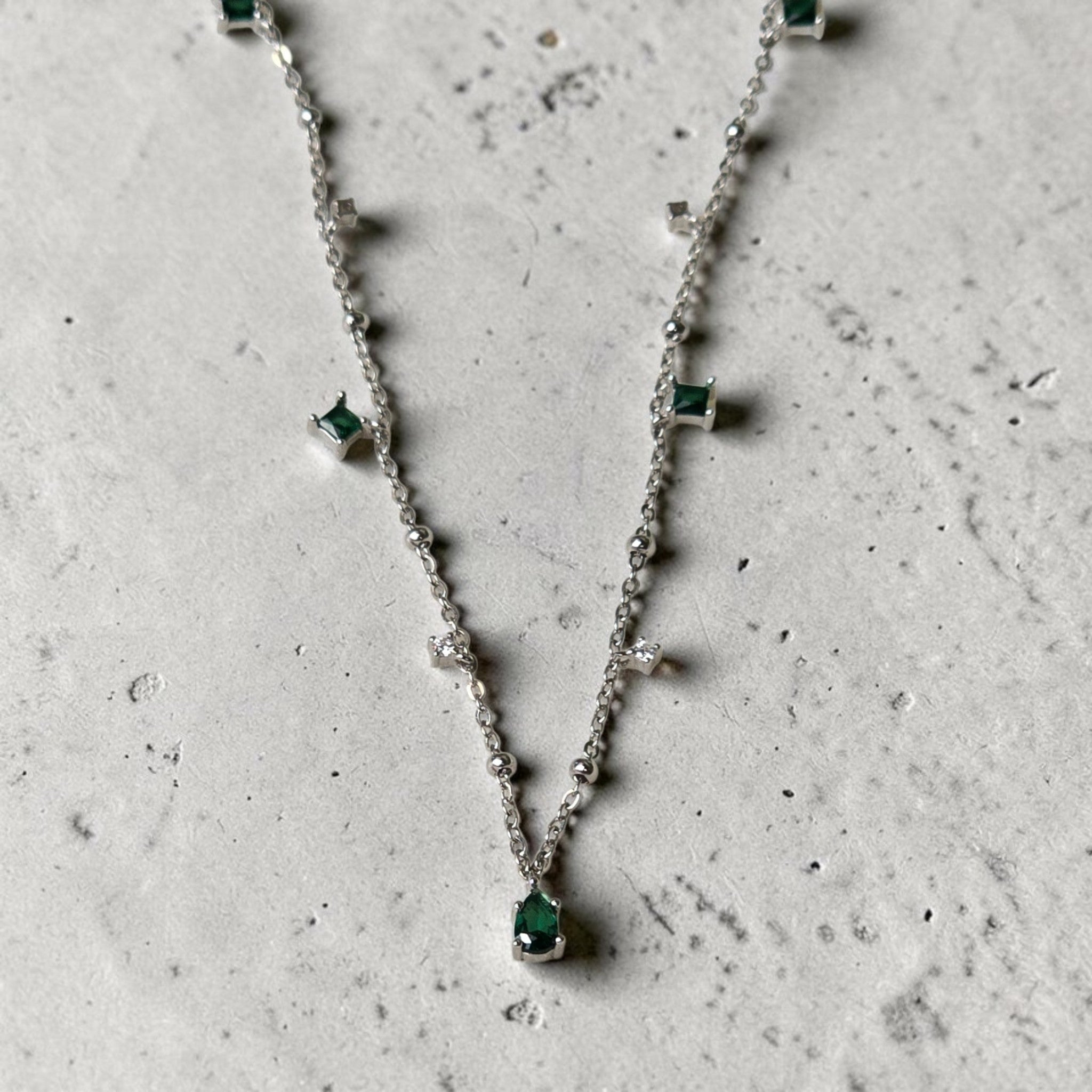reveriebygemma sterling silver choker with pear-cut emerald and cubic zirconia tassel charms on a marble surface