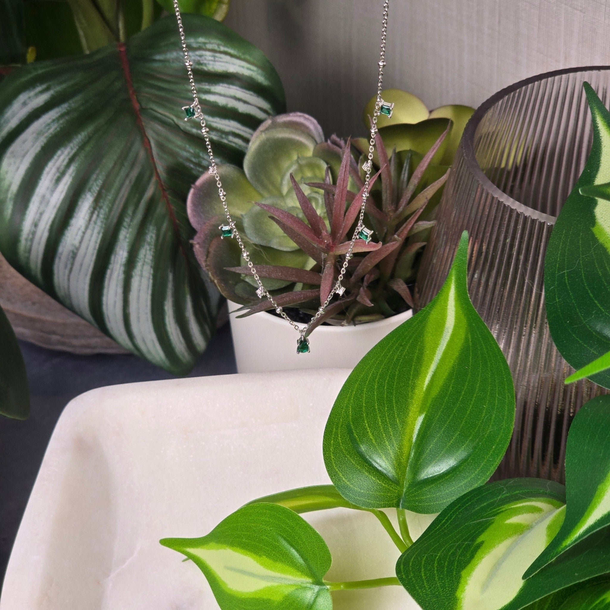 reveriebygemma sterling silver choker with emerald and cubic zirconia tassel charms, displayed among lush houseplants.
