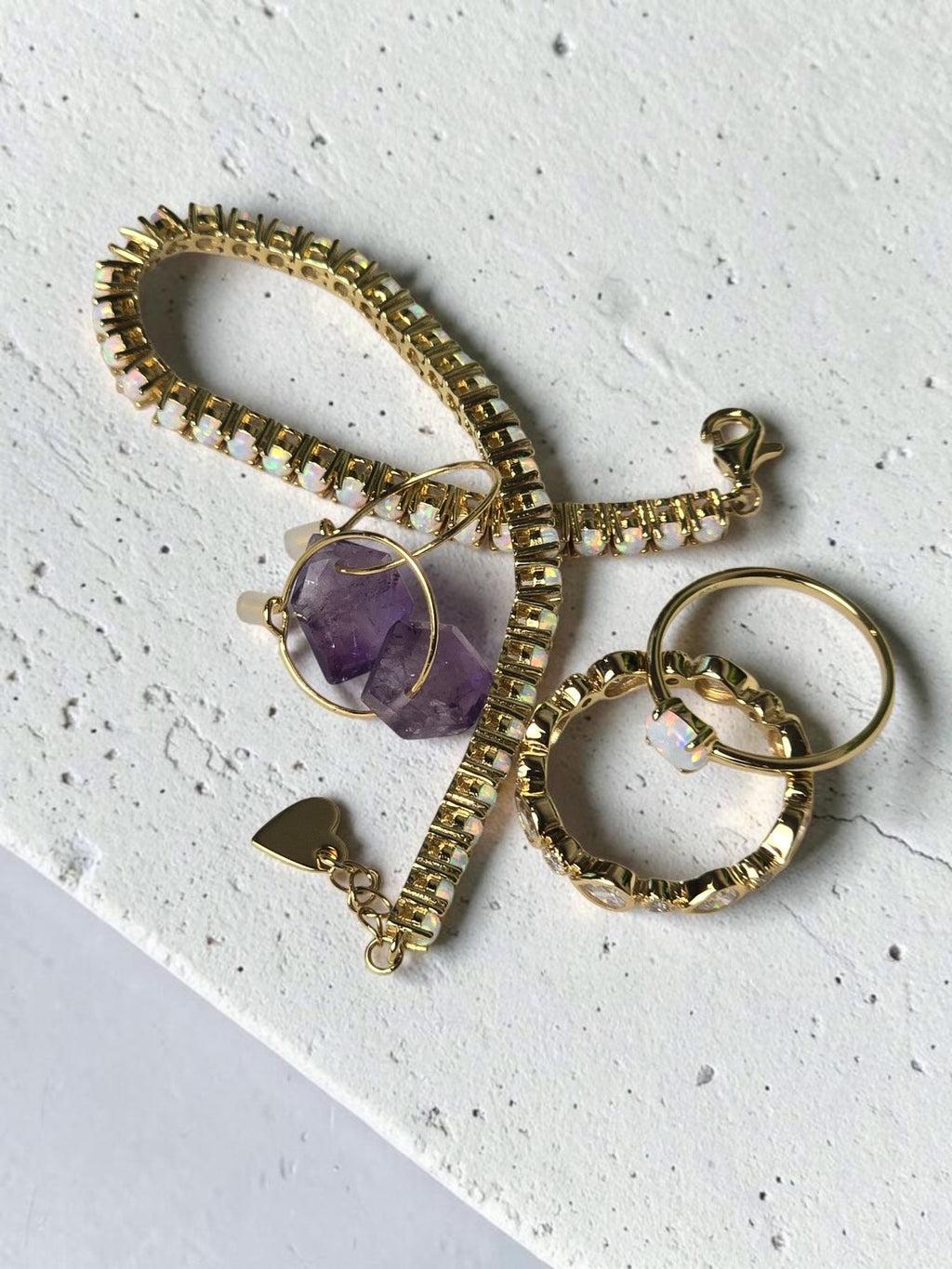 reveriebygemma fire opal stacking ring with gold tennis bracelet and amethyst hoop earrings on marble surface