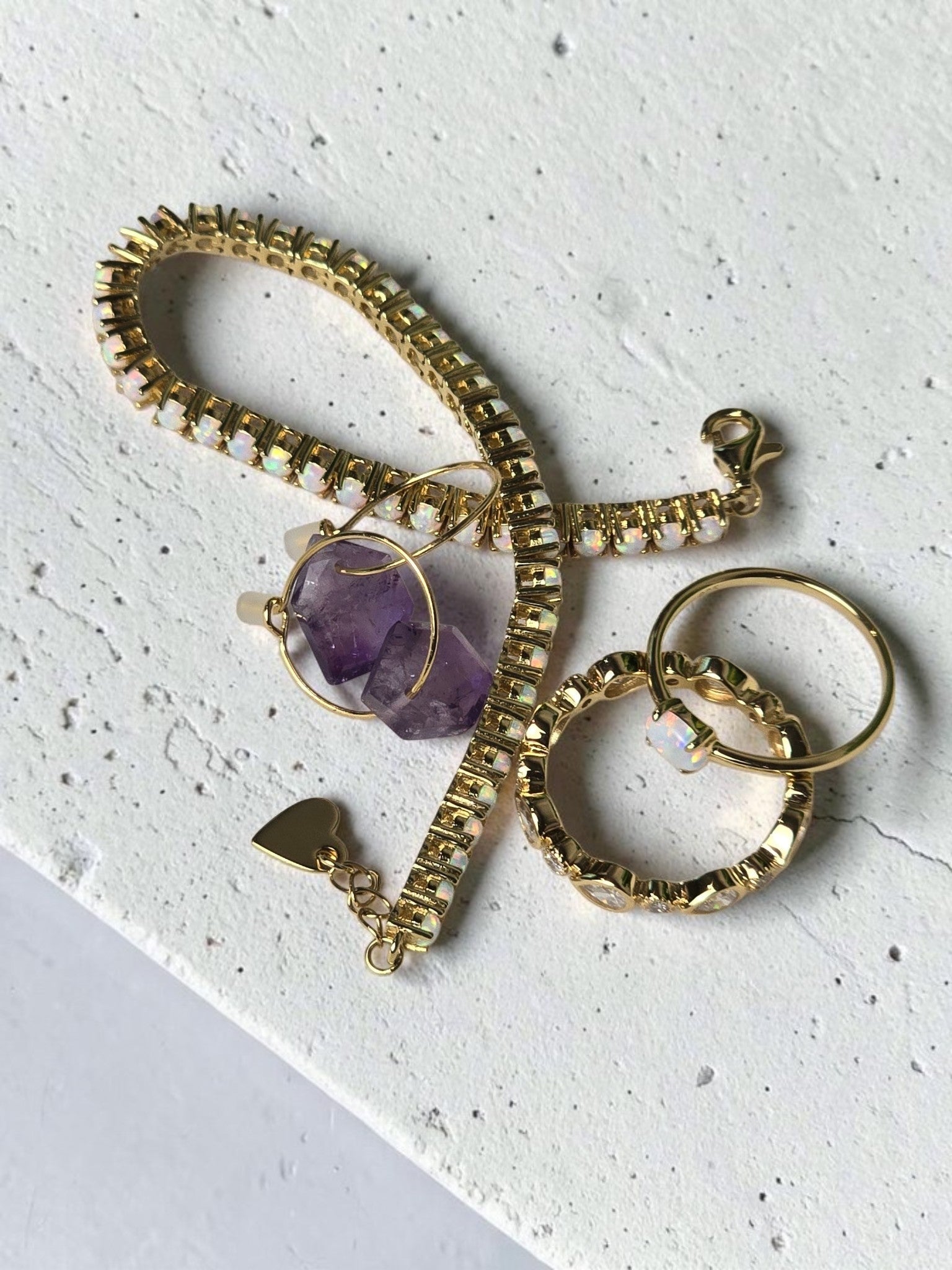 reveriebygemma fire opal stacking ring with gold tennis bracelet and amethyst hoop earrings on marble surface