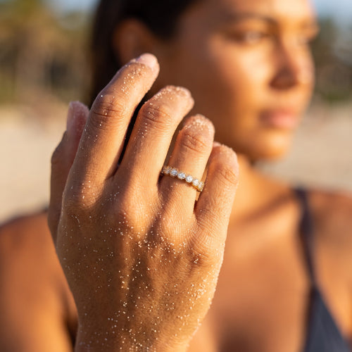 reveriebygemma gold plated sterling silver eternity band with bezel-set cubic zirconia on a woman's hand at the beach