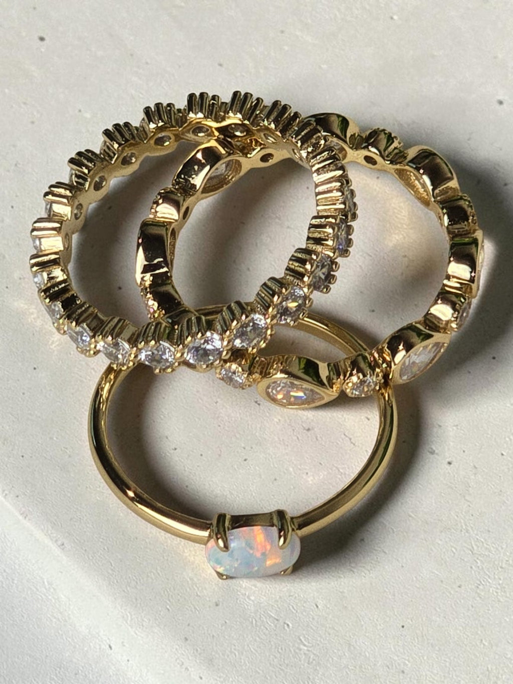 reveriebygemma gold bezel-set eternity band with cubic zirconia stacked with an opal ring on a white marble surface