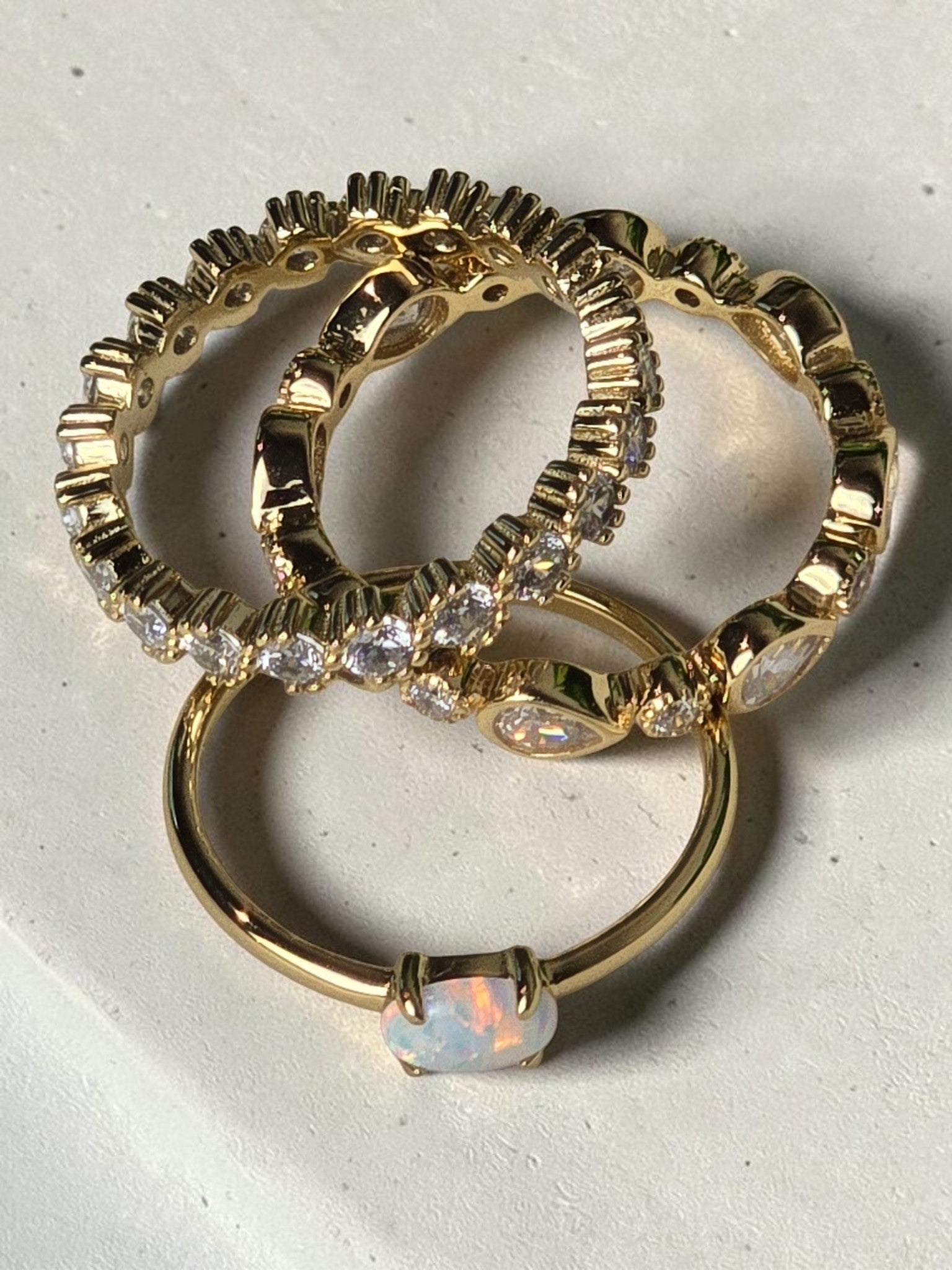 reveriebygemma gold bezel-set eternity band with cubic zirconia stacked with an opal ring on a white marble surface
