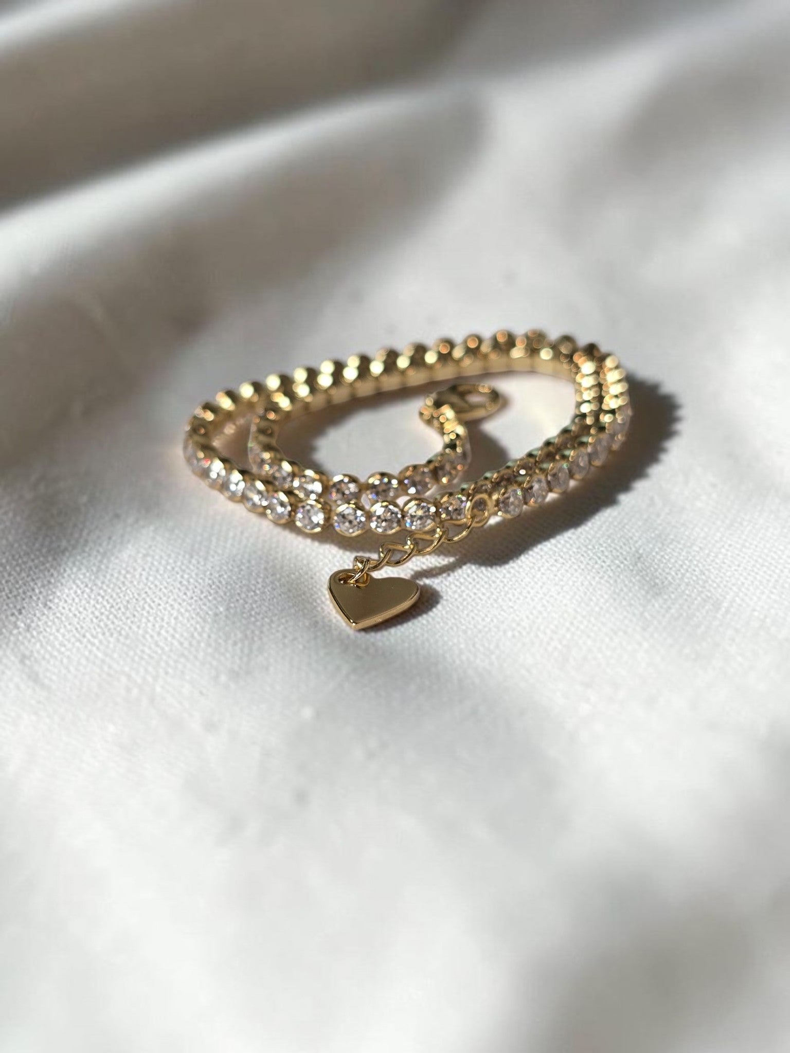 reveriebygemma 14kt gold plated sterling silver tennis anklet with cubic zirconia stones and a heart charm dangle.
