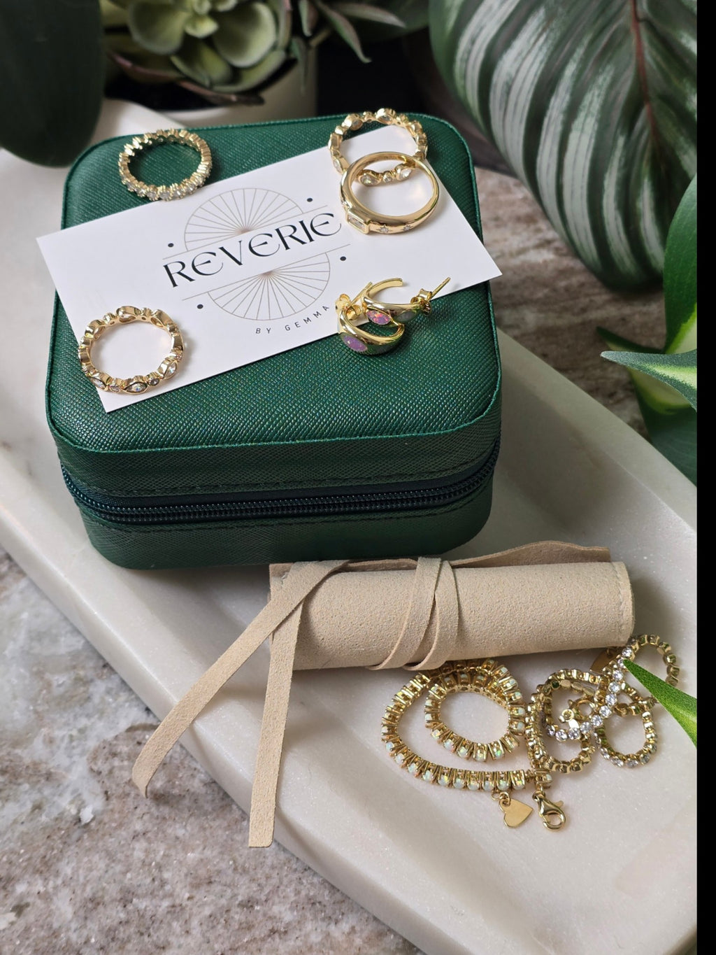 reveriebygemma jewelry collection featuring gold rings and earrings displayed on a green box and marble tray
