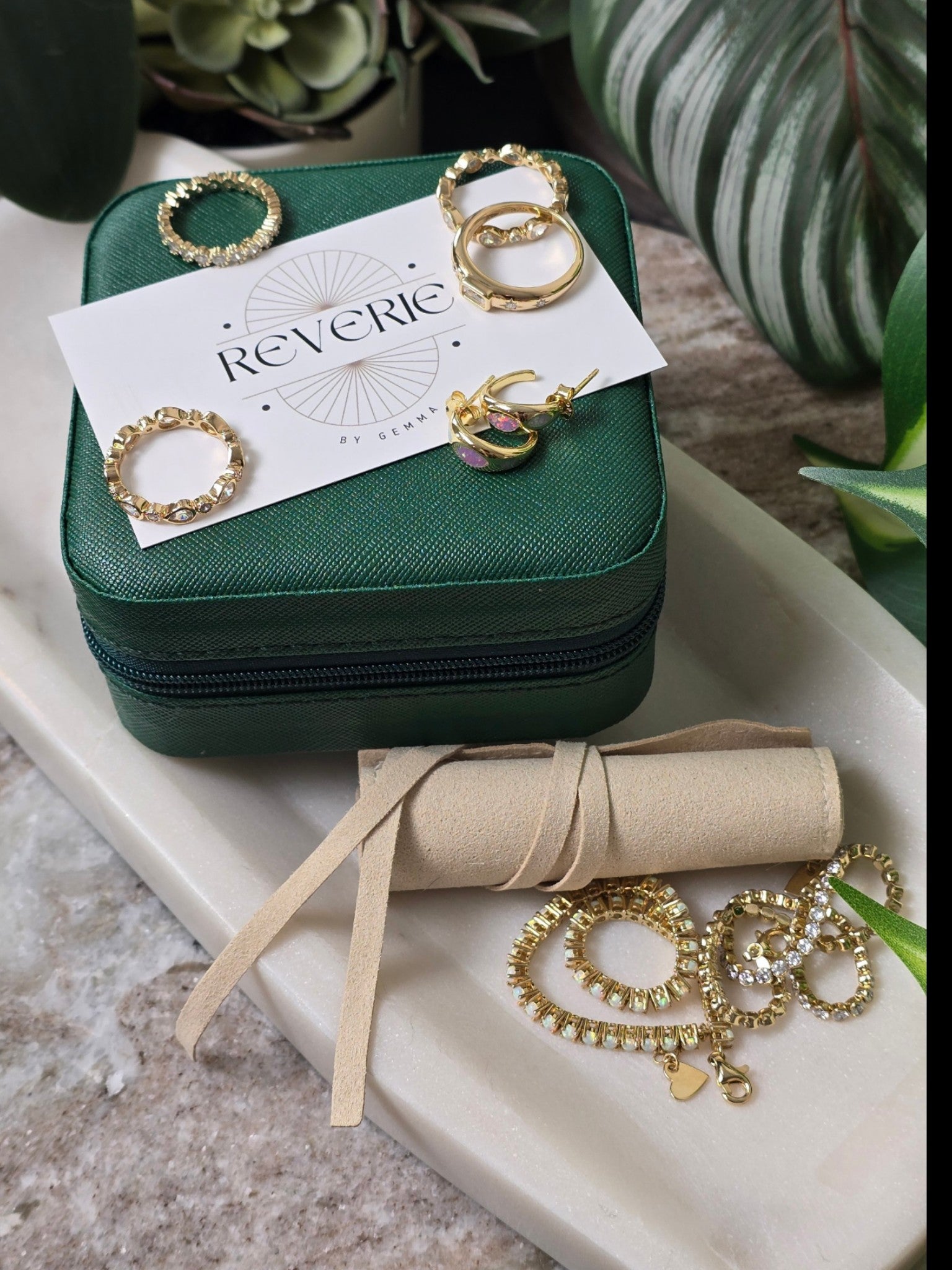 reveriebygemma jewelry collection featuring gold rings and earrings displayed on a green box and marble tray