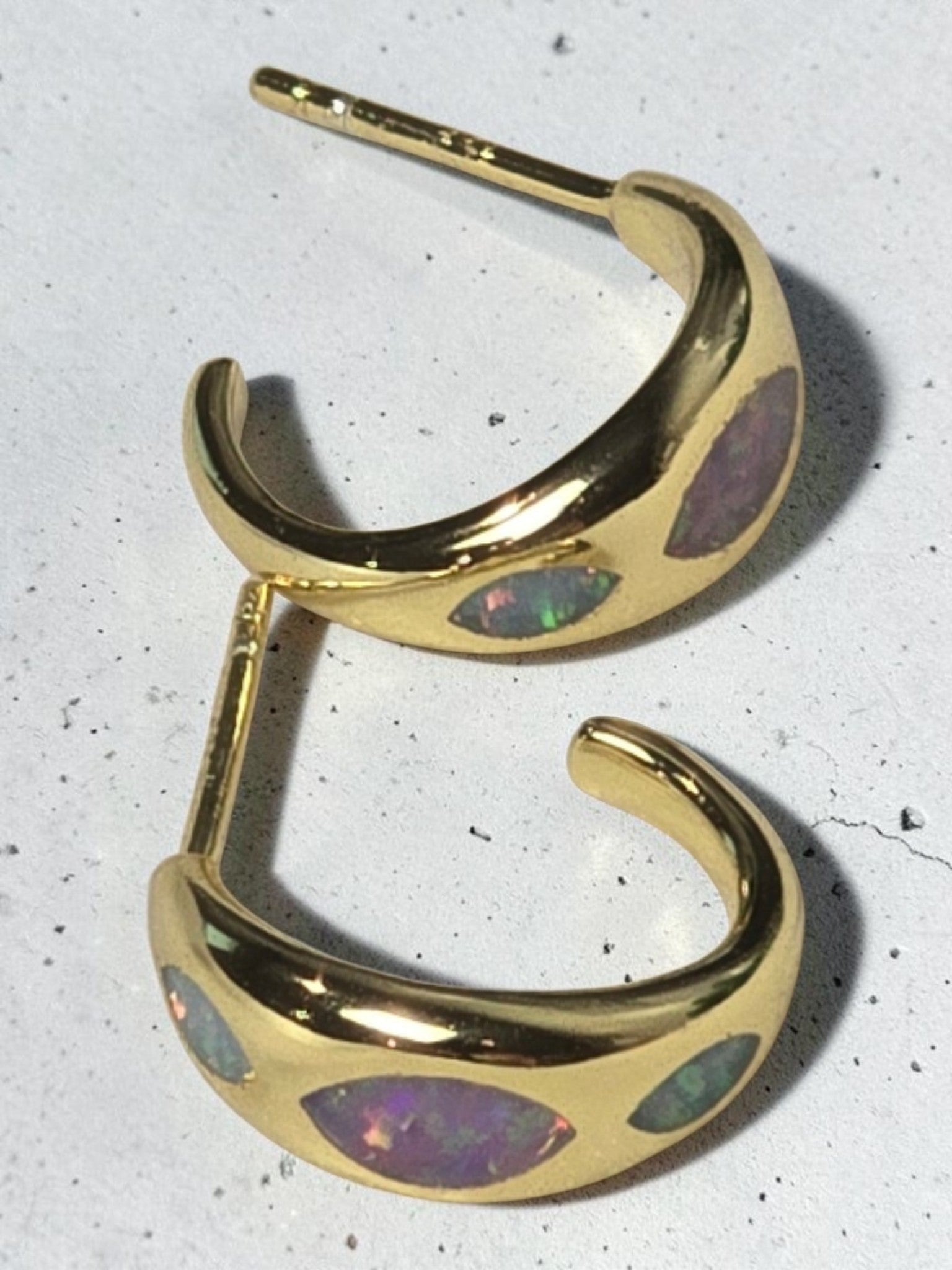 reveriebygemma 18kt gold vermeil huggie hoops featuring marquise-shaped iridescent opal inlays on a white surface.