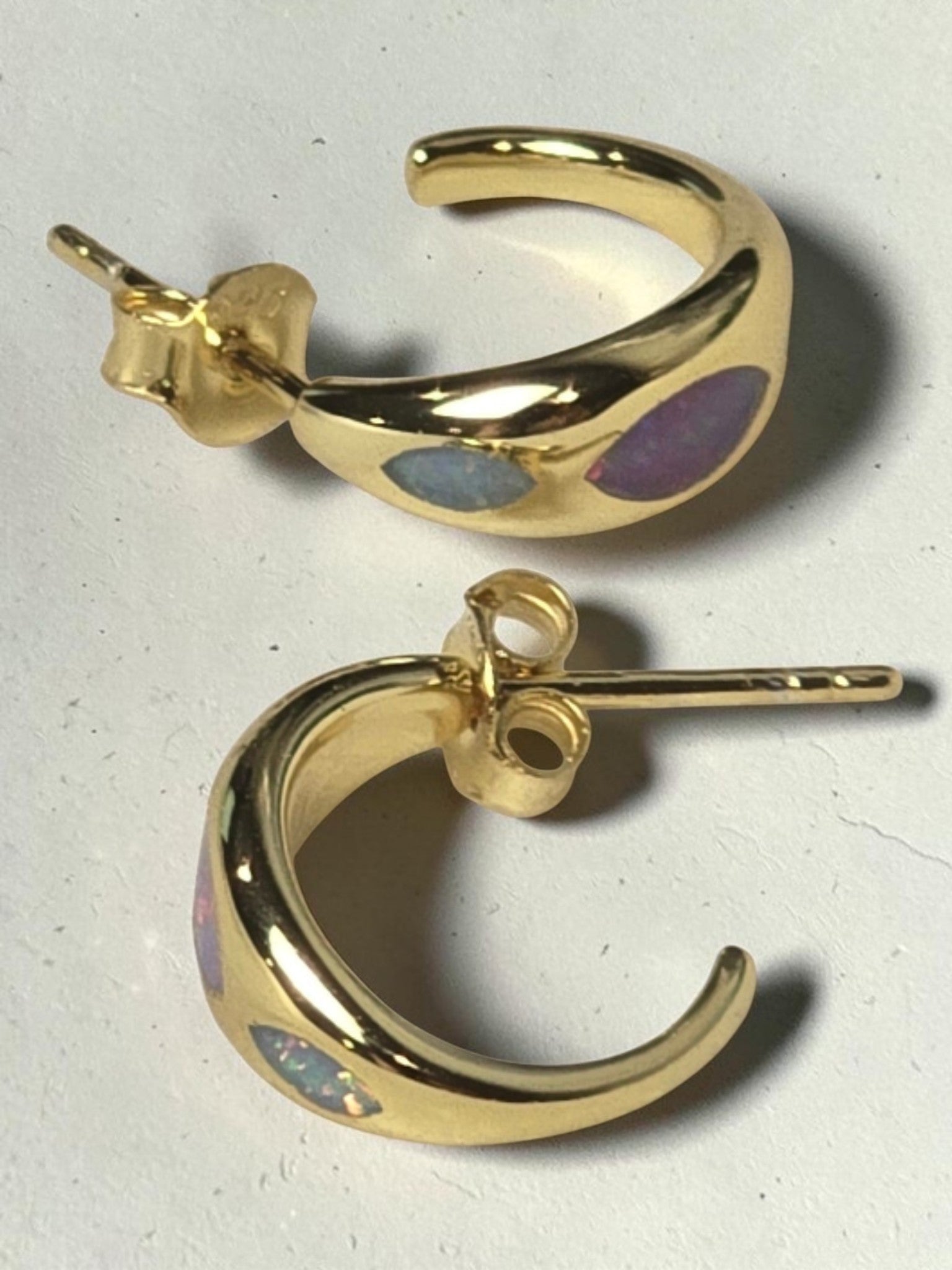 reveriebygemma 18kt gold vermeil huggie hoop earrings with iridescent marquise-shaped opal inlays on a white surface.