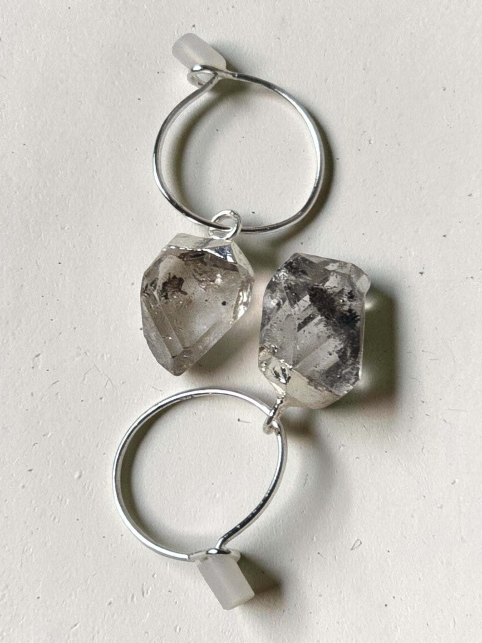 reveriebygemma sterling silver mini hoop earrings featuring raw-cut Herkimer diamond quartz crystals on a marble surface.