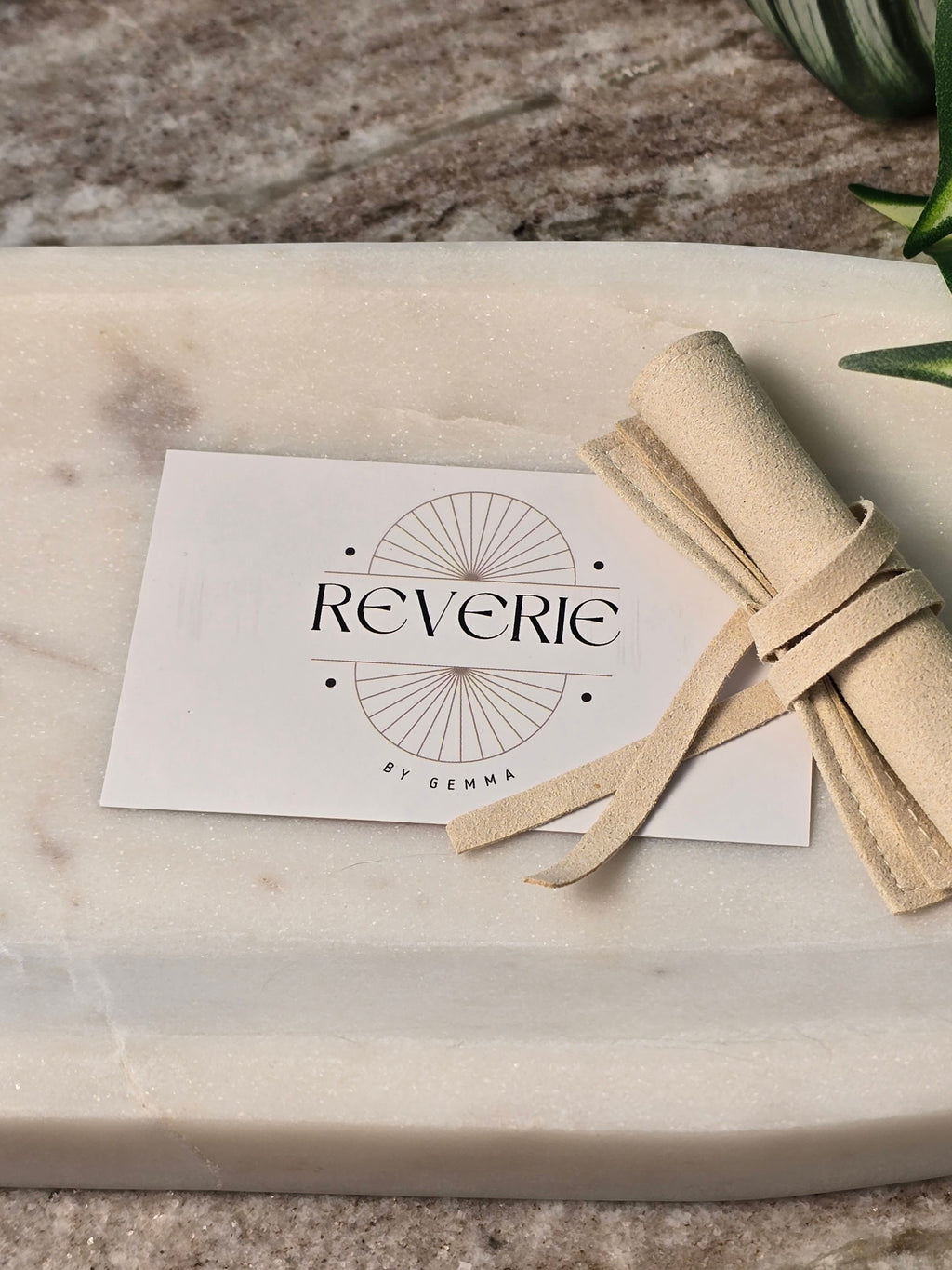 reveriebygemma branded card and beige velvet jewelry pouch on a marble surface for a premium unboxing experience