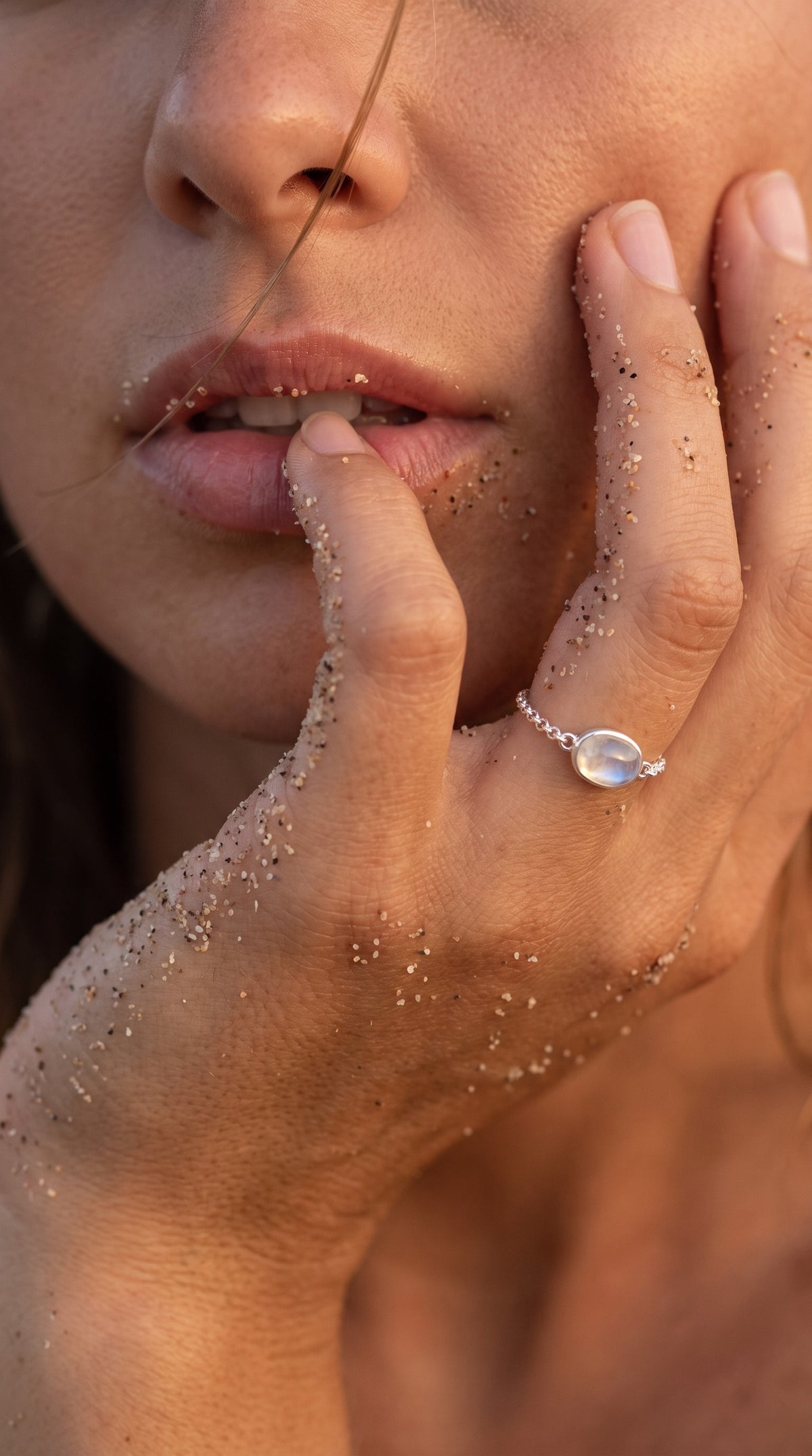 reveriebygemma adjustable sterling silver chain ring with an oval moonstone cabochon on a model's sandy hand