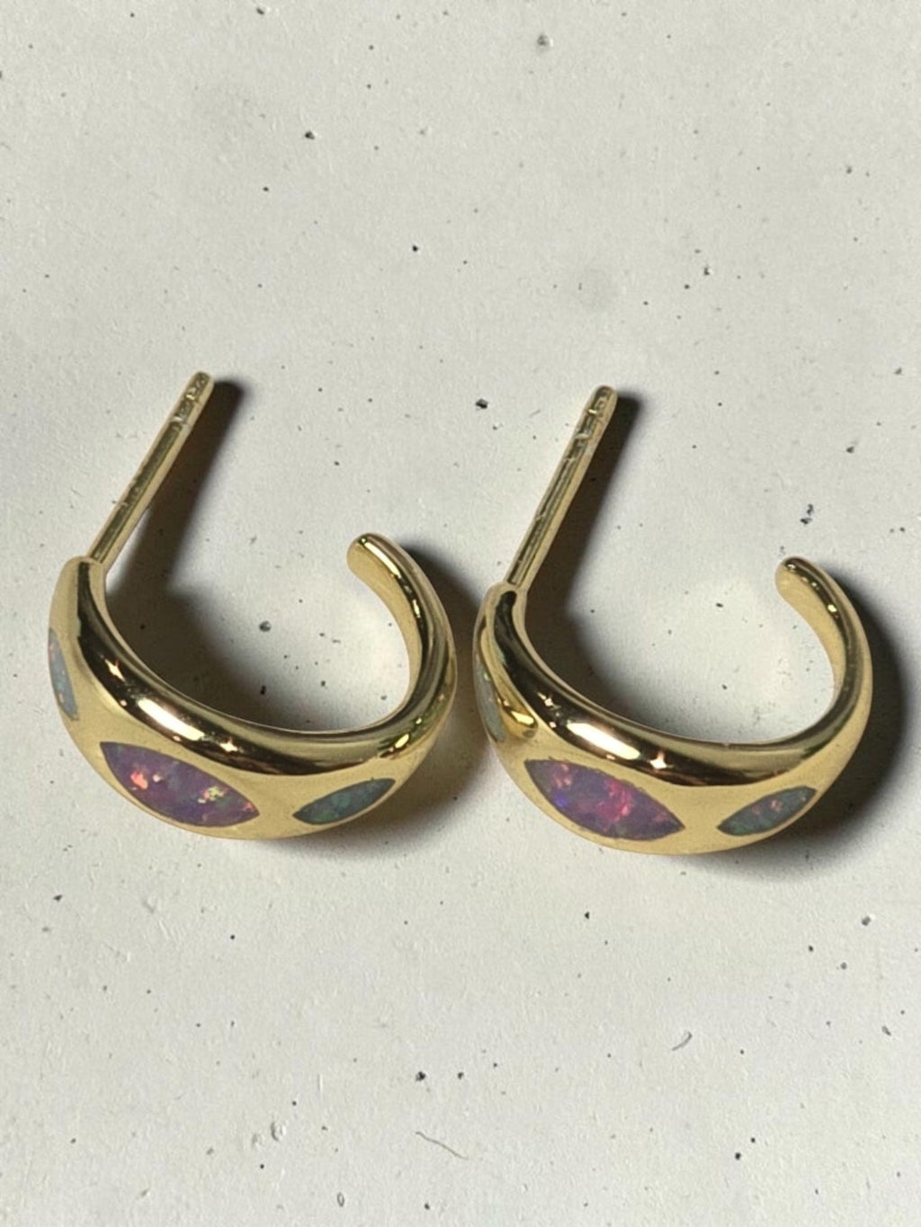 reveriebygemma 18kt gold vermeil huggie hoops featuring marquise-shaped iridescent opal inlays on a white surface.